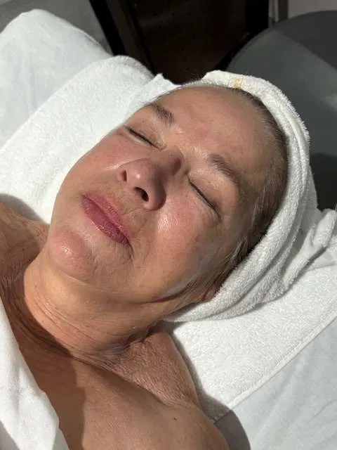 A client resting on the treatment bed with a warm towel turban after a facial &mdash; soft lighting in Holland's studio